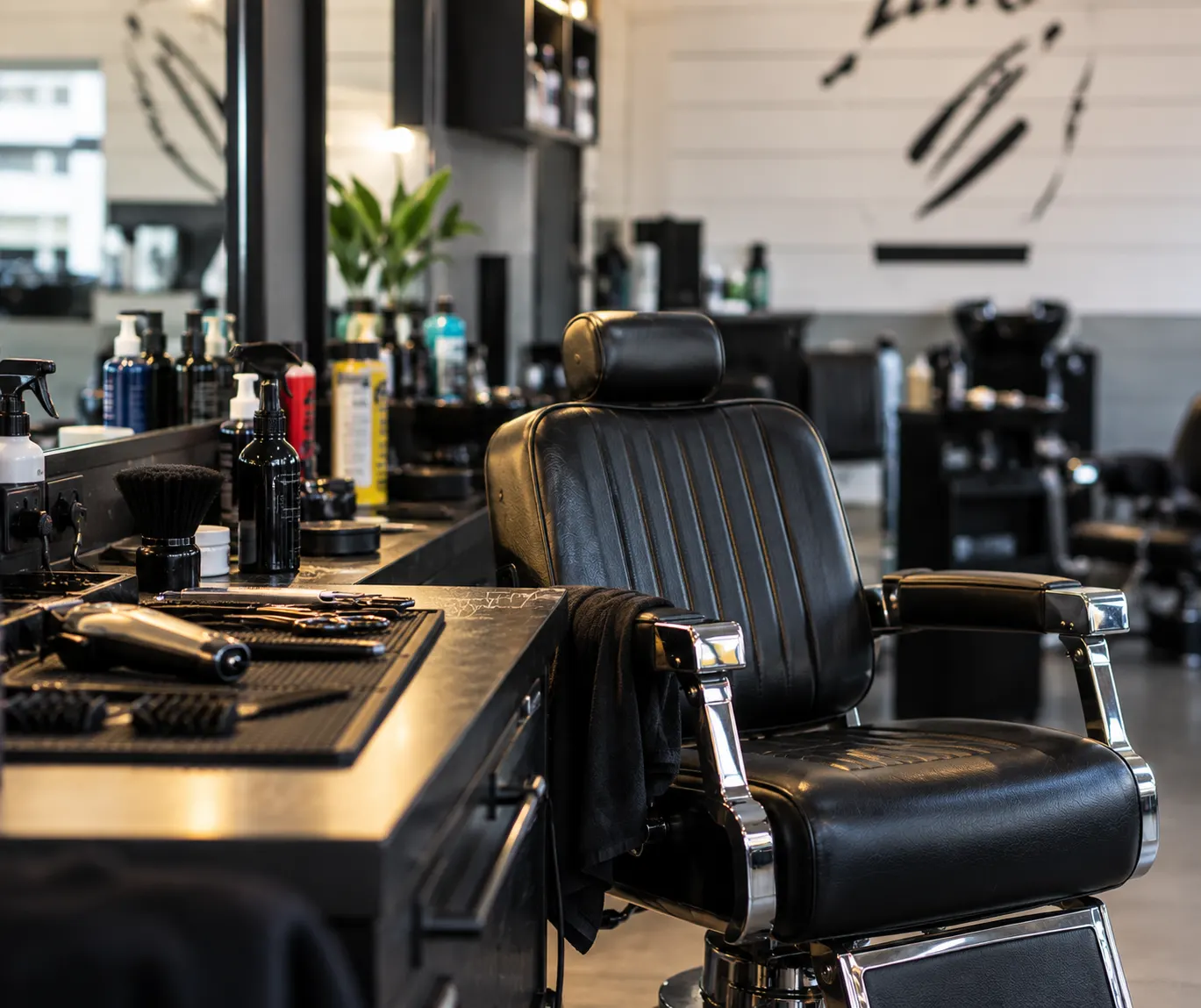 A black leather barber's chair beside a station of clippers and products